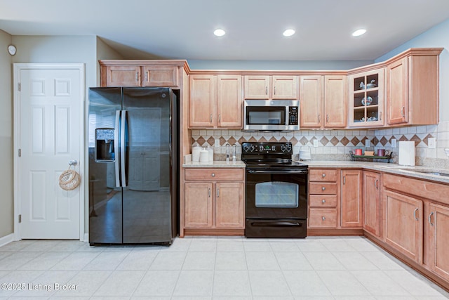 kitchen with tasteful backsplash, glass insert cabinets, black appliances, and light stone counters