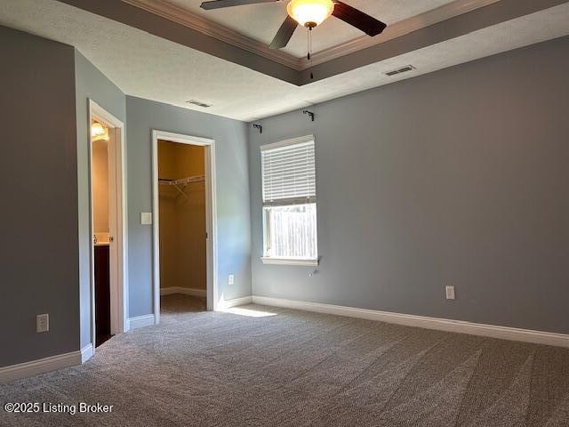 unfurnished bedroom featuring visible vents, baseboards, crown molding, a tray ceiling, and carpet floors