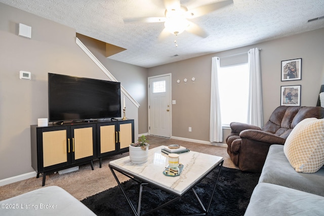 living room featuring visible vents, baseboards, a ceiling fan, a textured ceiling, and light carpet