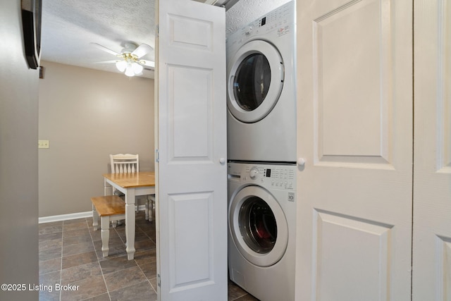 laundry room with laundry area, stone finish floor, a ceiling fan, baseboards, and stacked washer / drying machine