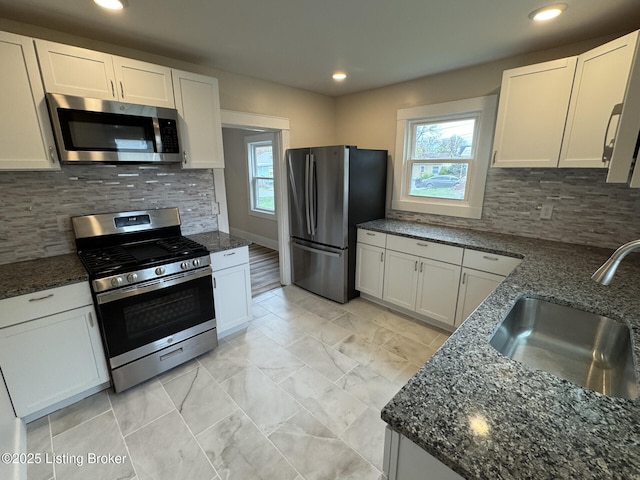 kitchen featuring dark stone counters, tasteful backsplash, white cabinetry, a sink, and stainless steel appliances