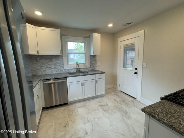kitchen featuring tasteful backsplash, visible vents, dark stone counters, stainless steel appliances, and a sink