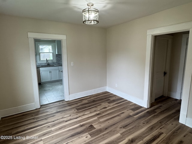 unfurnished dining area featuring a sink, baseboards, a notable chandelier, and dark wood-type flooring