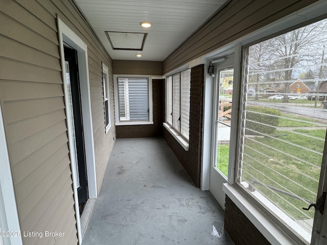 unfurnished sunroom with wooden walls, unfinished concrete flooring, and a wealth of natural light