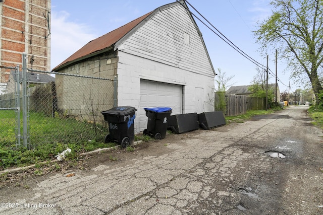 view of home's exterior featuring concrete block siding, an outdoor structure, fence, and a detached garage
