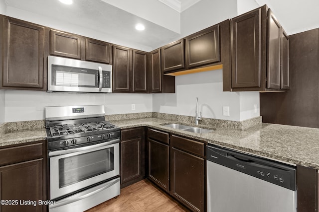 kitchen featuring a sink, dark brown cabinetry, crown molding, light stone countertops, and stainless steel appliances