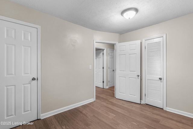 unfurnished bedroom with baseboards, wood finished floors, a textured ceiling, and a closet