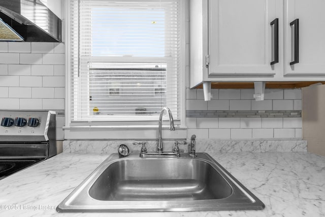 kitchen with wall chimney exhaust hood, a sink, decorative backsplash, light stone counters, and electric stove