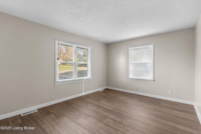 spare room with baseboards, wood finished floors, visible vents, and a textured ceiling