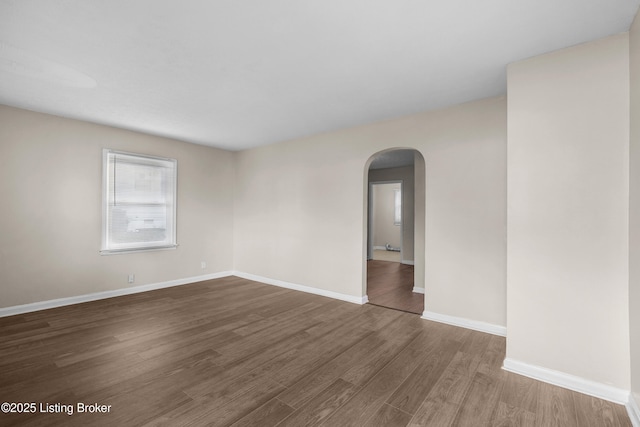 spare room with arched walkways, wood finished floors, and baseboards
