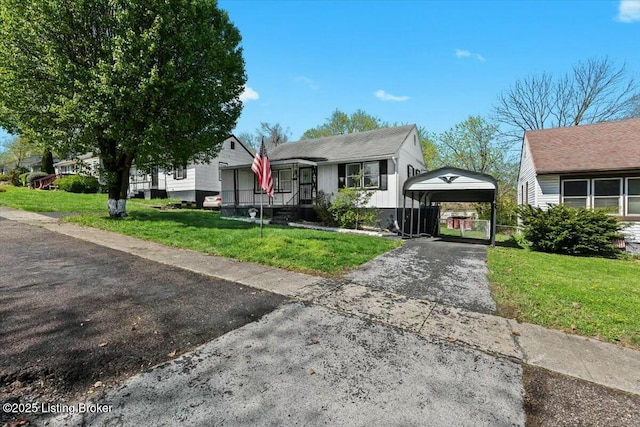 view of front facade featuring a detached carport, driveway, a front yard, and a gate