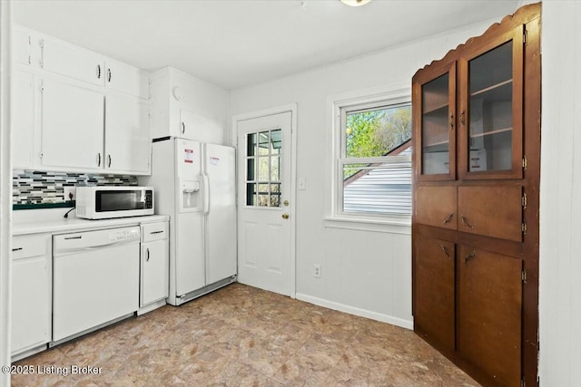 kitchen featuring baseboards, light countertops, white appliances, white cabinetry, and backsplash