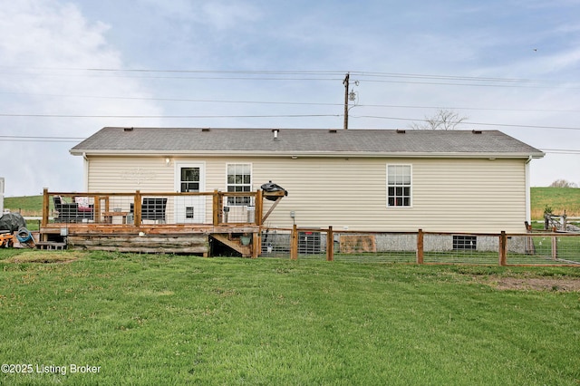 rear view of house featuring fence, a deck, and a lawn