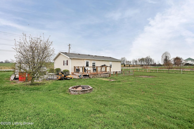 rear view of house with an outdoor fire pit, fence, a wooden deck, and a lawn