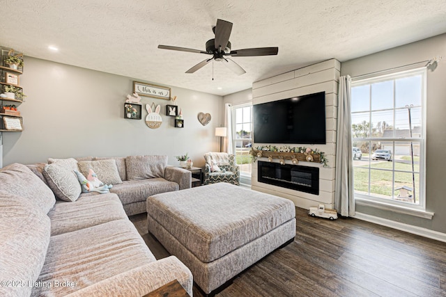 living area with a ceiling fan, a glass covered fireplace, a textured ceiling, and dark wood-style flooring