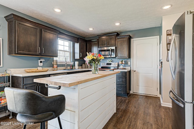 kitchen featuring a center island, butcher block countertops, dark brown cabinetry, dark wood finished floors, and appliances with stainless steel finishes