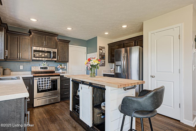 kitchen featuring wooden counters, a kitchen island, dark brown cabinetry, appliances with stainless steel finishes, and dark wood-style flooring