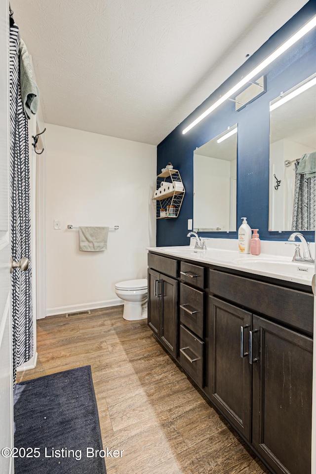 full bath with double vanity, wood finished floors, toilet, and a sink