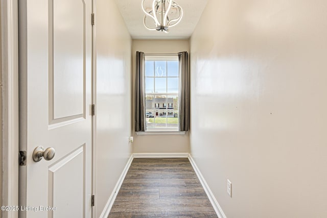 doorway to outside with dark wood finished floors, baseboards, and an inviting chandelier