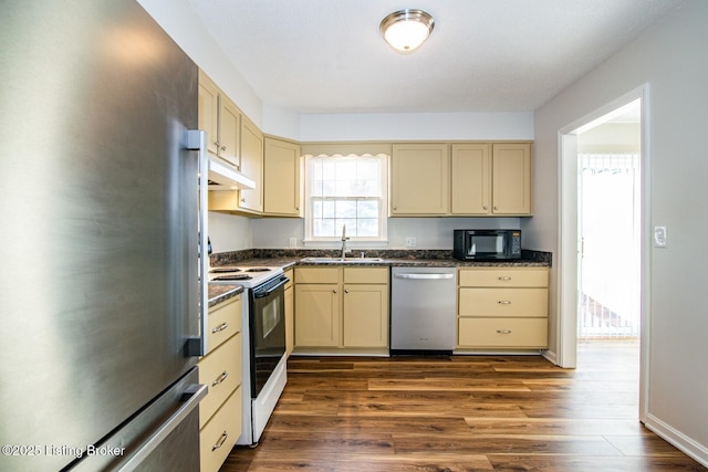 kitchen with a sink, cream cabinets, dark countertops, and stainless steel appliances