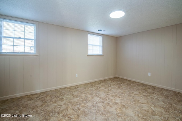 spare room featuring a textured ceiling, wooden walls, and visible vents