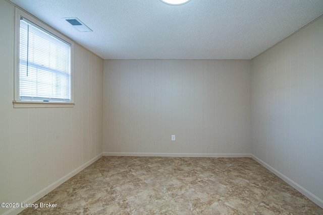 spare room featuring a textured ceiling, wood walls, and visible vents