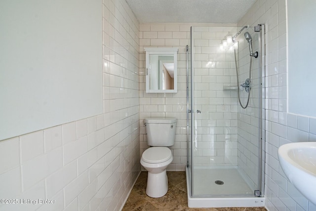 bathroom featuring a shower stall, a textured ceiling, toilet, a sink, and tile walls