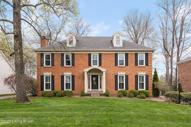 view of front facade with brick siding, a chimney, and a front lawn