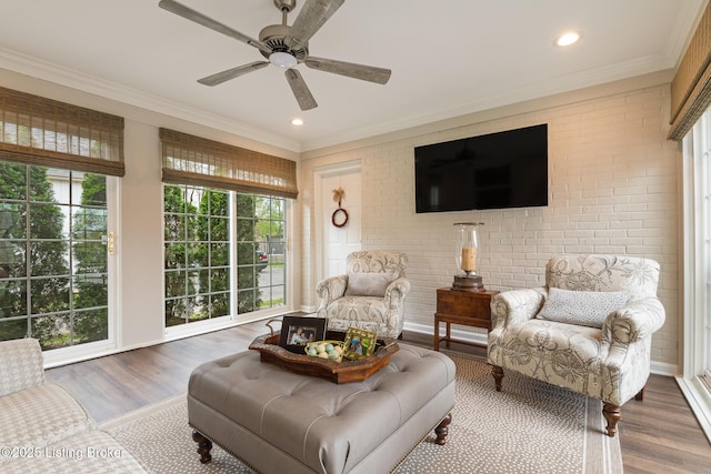 living area featuring crown molding, ceiling fan, brick wall, and wood finished floors