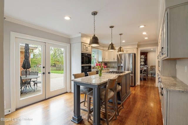 kitchen with appliances with stainless steel finishes, a kitchen bar, crown molding, light wood finished floors, and light stone countertops