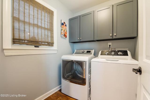 clothes washing area featuring wood finished floors, washing machine and clothes dryer, baseboards, and cabinet space