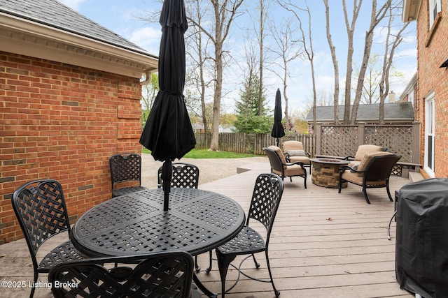 wooden deck featuring a grill, outdoor dining area, a fenced backyard, and a fire pit
