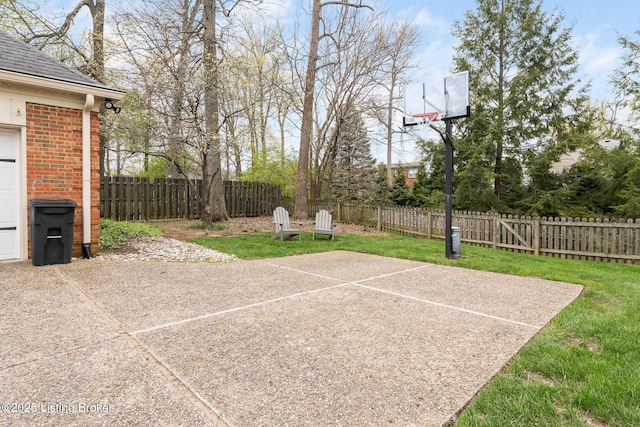 view of basketball court featuring fence, a yard, and basketball hoop