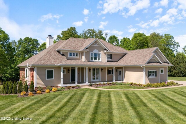 traditional home with roof with shingles, covered porch, a chimney, and a front lawn