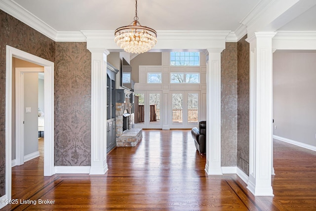 unfurnished living room featuring an inviting chandelier, baseboards, decorative columns, and dark wood-style flooring