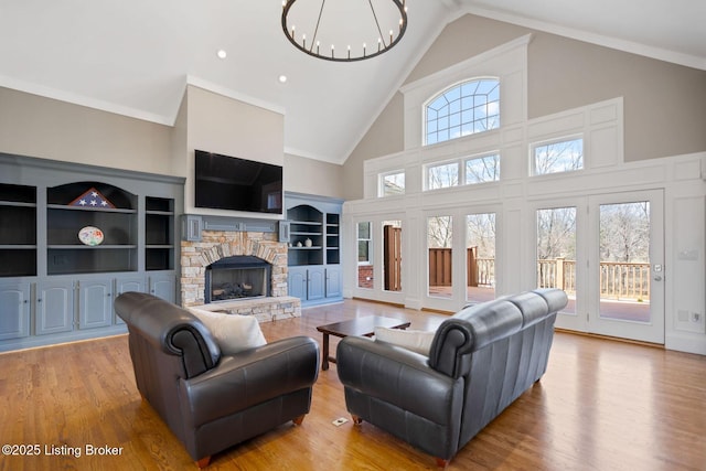 living area featuring high vaulted ceiling, a stone fireplace, wood finished floors, and a notable chandelier