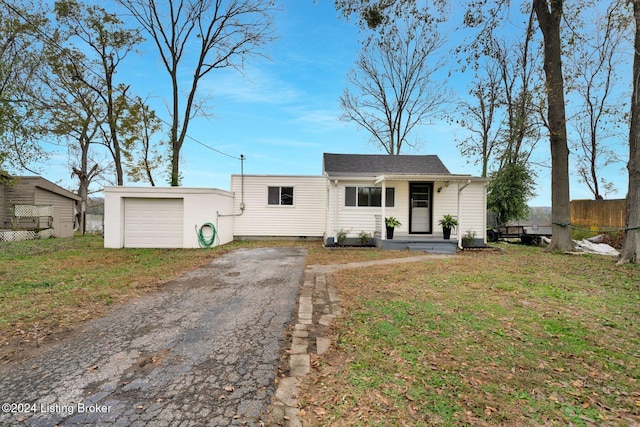 view of front of house with a front lawn, aphalt driveway, an outdoor structure, fence, and a garage