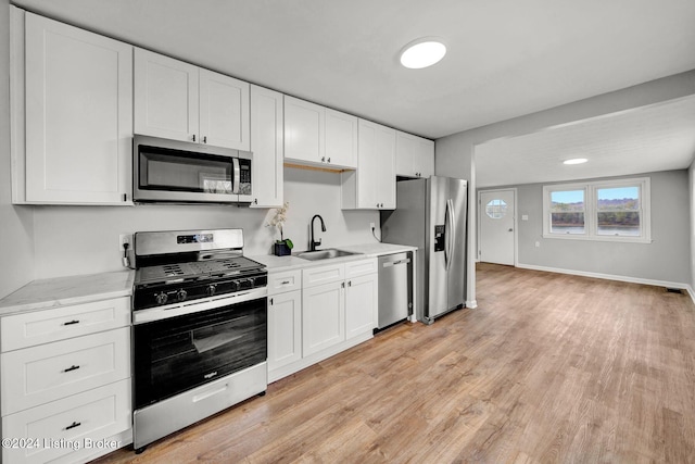 kitchen with a sink, stainless steel appliances, light wood-style flooring, baseboards, and white cabinetry