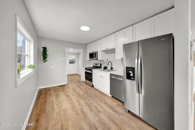 kitchen with white cabinets, a sink, baseboards, light wood-style floors, and appliances with stainless steel finishes