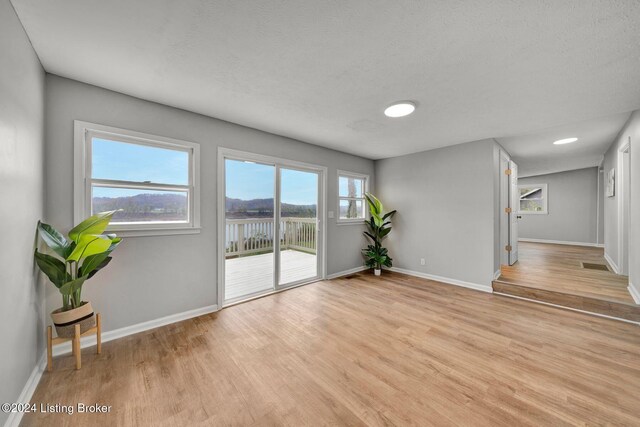 interior space featuring baseboards, visible vents, a textured ceiling, and light wood finished floors