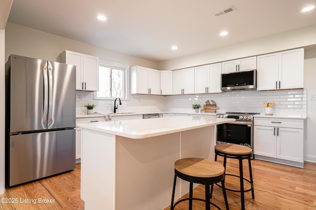 kitchen featuring a center island, light countertops, appliances with stainless steel finishes, a kitchen bar, and light wood-style flooring