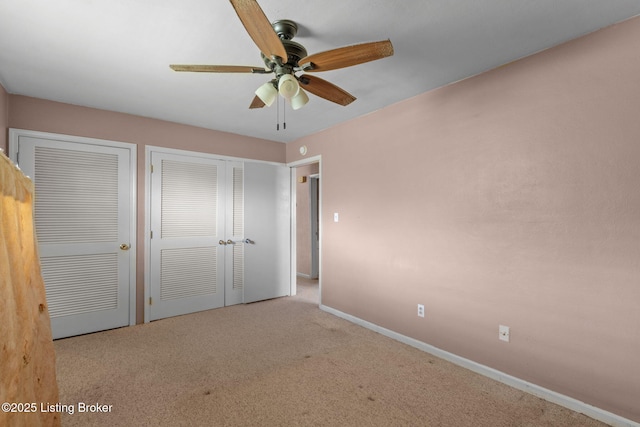 unfurnished bedroom with two closets, carpet flooring, baseboards, and a ceiling fan