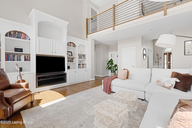 living area featuring a high ceiling, wood finished floors, baseboards, and built in shelves