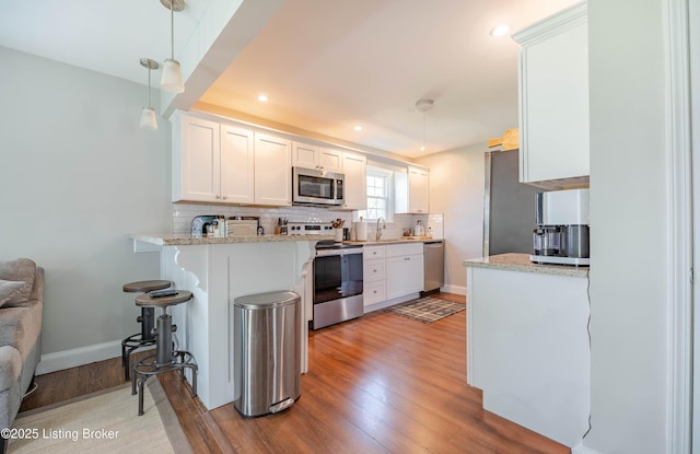 kitchen featuring tasteful backsplash, a peninsula, white cabinetry, light wood-style floors, and appliances with stainless steel finishes
