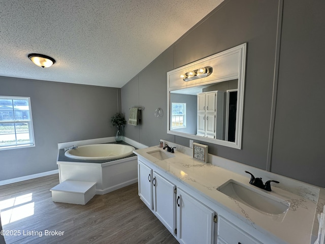 bathroom with a textured ceiling, wood finished floors, a sink, and vaulted ceiling