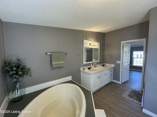 full bath featuring vanity, baseboards, a textured ceiling, a tub to relax in, and wood finished floors