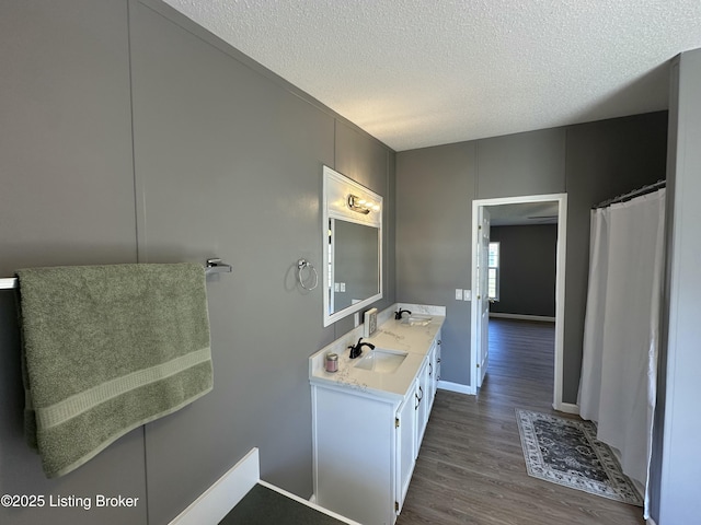 full bathroom with baseboards, a textured ceiling, a sink, and wood finished floors