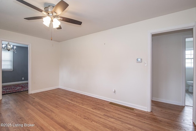 unfurnished room featuring light wood-style floors, visible vents, baseboards, and ceiling fan with notable chandelier