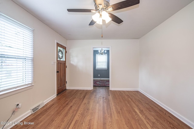 spare room featuring visible vents, baseboards, wood finished floors, and ceiling fan with notable chandelier