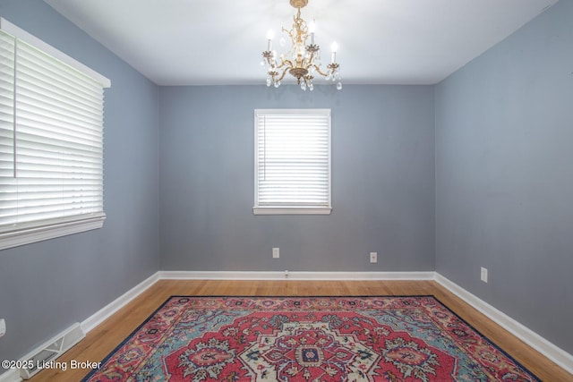 empty room featuring a chandelier, light wood-style floors, baseboards, and visible vents